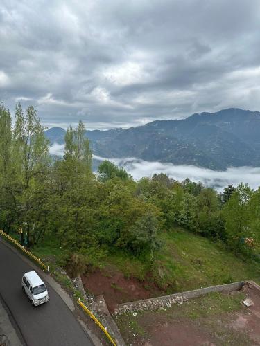 a white car driving down a road with clouds in the mountains at Shaiz Apartments Bhurban, Murree in Murree