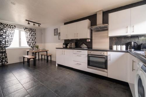 a kitchen with white cabinets and a table in it at Spacious 3 Bed House, 5mins to HS2/ NEC/Airport. in Marston Green