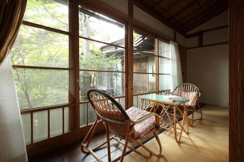 two chairs and a table in a room with windows at Tsuruya Ryokan in Karuizawa