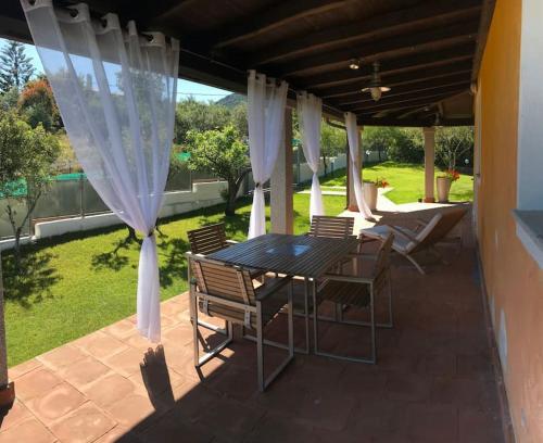 a table and chairs on a patio with white curtains at Splendida villa unifamiliare Posada in Torpè