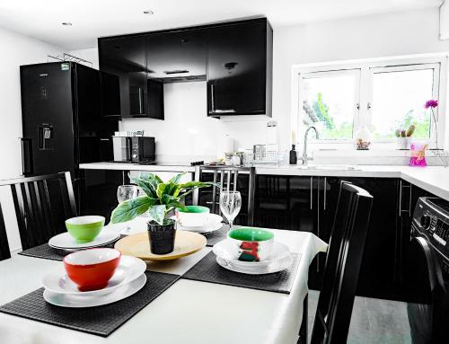 a kitchen with black cabinets and a table with plates and bowls at Charming London Home, Opp Arnos Grove Underground Station, Parking in New Southgate