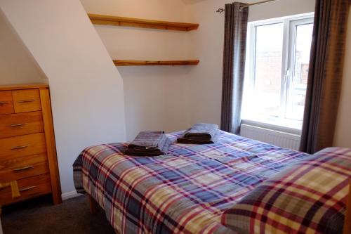 um quarto com uma cama com um cobertor xadrez e uma janela em Cosy Cottage to Relax or Explore em Mistley
