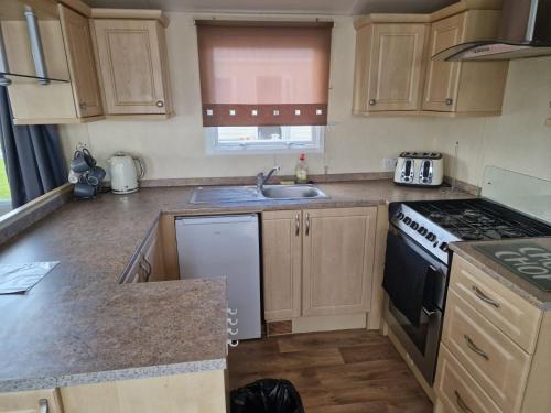 uma cozinha com um lavatório e um fogão forno superior em 6 berth Seawick Caravan Park, St Osyth em Colchester