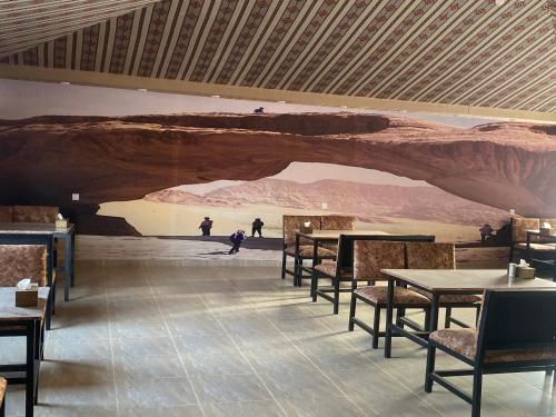 una sala da pranzo con tavoli e un murale di un deserto di Omar Camp Wadi Rum a Disah
