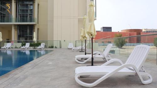 a row of lounge chairs and umbrellas next to a pool at Warmcloud 2BR Oasis Home in Masdar - Relaxing Stay Near Masdar Park & City Centre in Abu Dhabi