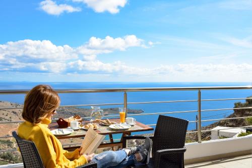 a woman sitting at a table reading a book on a balcony at Livaniana Panoramic View House 1 in Livanianá