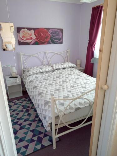 ein Schlafzimmer mit einem weißen Bett mit Blumen an der Wand in der Unterkunft Chalet at California Sands in Scratby