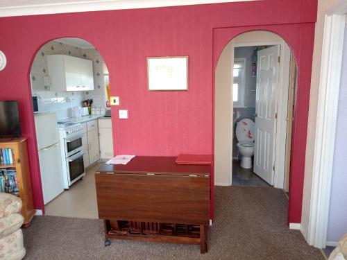 uma cozinha com paredes cor-de-rosa e uma mesa num quarto em Chalet at California Sands em Scratby