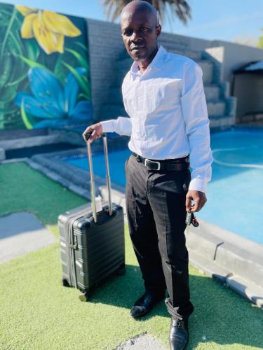 a man standing with a suitcase in front of a pool at Evans Village - Apartments & Spa in Johannesburg