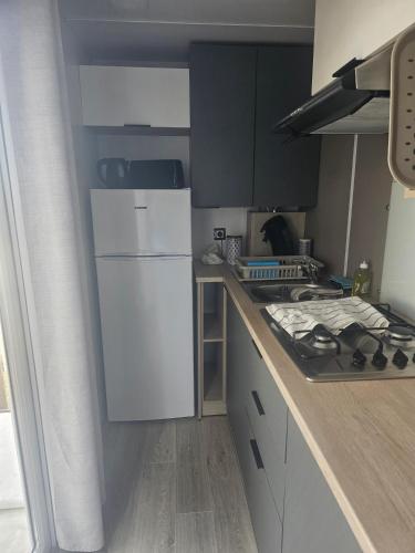 Il comprend une cuisine équipée d'un réfrigérateur blanc et d'une cuisinière. dans l'établissement Charmant mobil home premium L048, à Narbonne