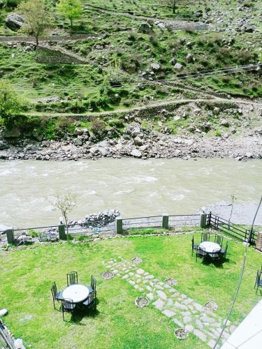 two picnic tables in the grass next to a river at BONO MOTELS in Nārān
