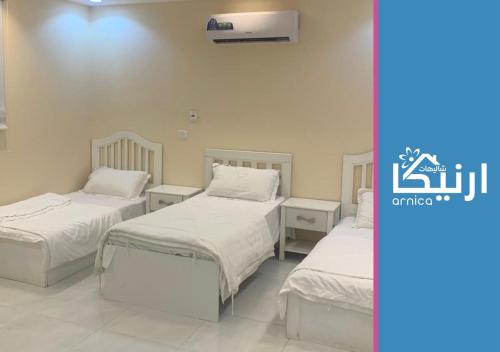 2 camas en una habitación con sábanas y almohadas blancas en شالية ارنيكا en As Sayl aş Şaghīr