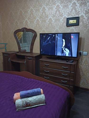 ein Schlafzimmer mit einem TV und einer Kommode mit einem Bett in der Unterkunft Трешка Саулет 11 in Qysylorda