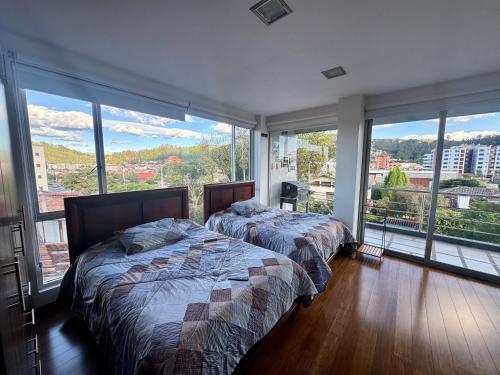two beds in a bedroom with large windows at Maravilloso departamento con moto electricá in Cuenca