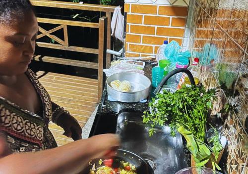 a woman preparing food on top of a stove at Casa DaJu - 6 minutos do cais da Vila do Abraão em Ilha Grande - Angra dos Reis in Angra dos Reis