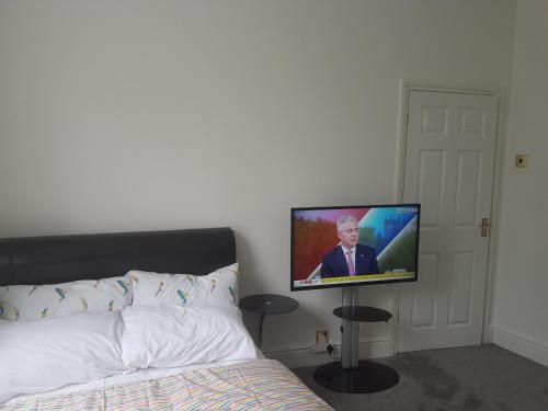 a flat screen tv hanging on a wall next to a bed at A Quiet & Comfortable 4 Bedroom house in Manchester