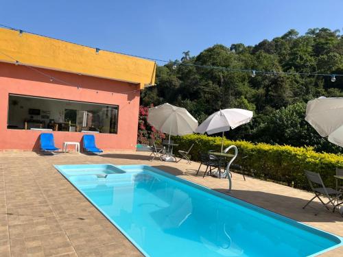 uma piscina com cadeiras e guarda-sóis ao lado de um edifício em POUSADA PE NA TERRA EM GUARAREMA em Guararema