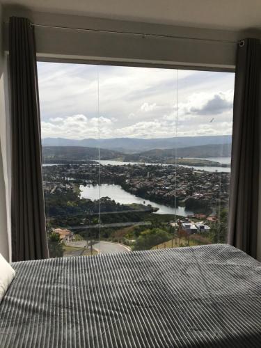 a bedroom with a large window with a view of a river at Suíte no Mirante em Escarpas in Capitólio