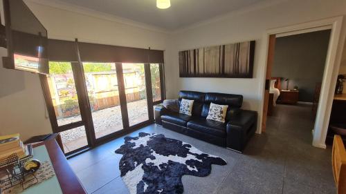 a living room with a black leather couch and a rug at Red Ochre - Large Apartment with Private Courtyard in Port Pirie