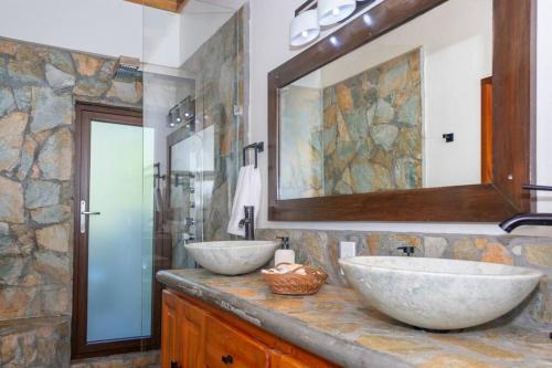 La salle de bains est pourvue de 2 lavabos et d'un mur en pierre. dans l'établissement Apricari House Stunning Views 3 BDRM and Pool, à Roatán