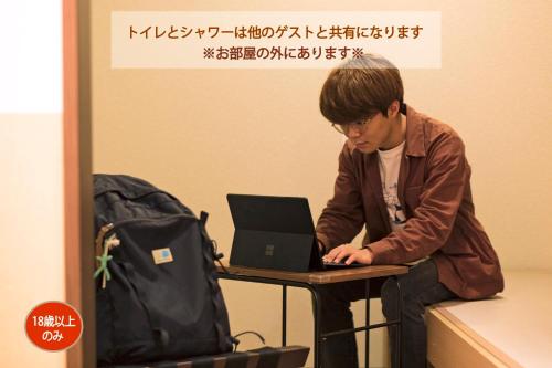 a man sitting at a table with a laptop computer at Wild Cherry Blossom-HOSTEL,TOKYO KOGANEI- in Koganei