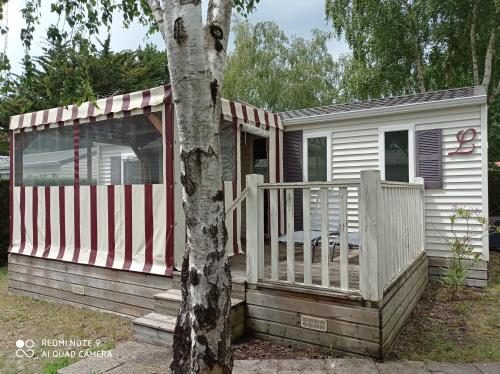 a small white house with a porch and a tree at Mobil-home in La Bernerie-en-Retz