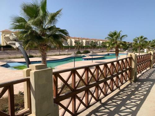 a wooden fence with two swimming pools with palm trees at luxury 3BD villa in Stella Heights - North Coast فيلا فاخره ستيلا هايتس الساحل الشمالي in El Alamein