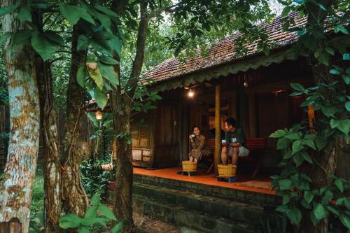two people sitting on a porch of a cabin in the woods at Chay Lap Farmstay Phong Nha in Ðá Lòn