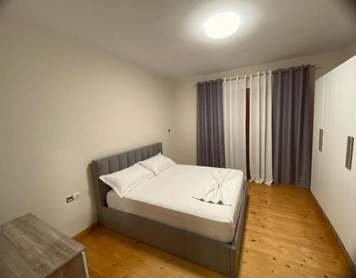 a bedroom with a bed with white sheets and a wooden floor at Cozy Corner - Apartment in Korça in Korçë