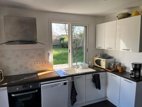 une cuisine avec des armoires blanches, un évier et une fenêtre dans l'établissement Charmante maison landaise, à Soustons