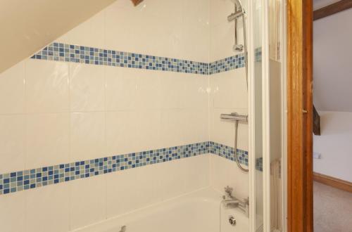 a bathroom with a tub and a shower with blue tiles at The Coach House in Porlock