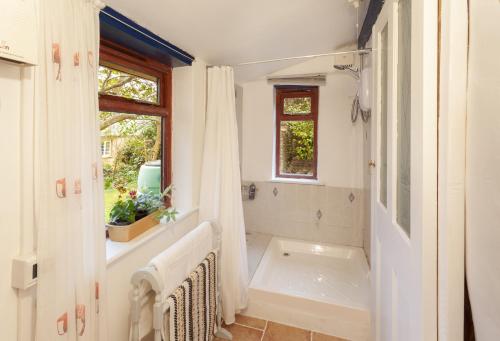 een witte badkamer met een bad en een raam bij Garden Cottage, Wiveliscombe in Wiveliscombe