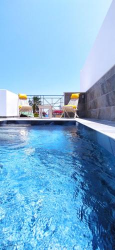 a swimming pool with chairs and blue water at Chariot Apartments Santorini in Kamari
