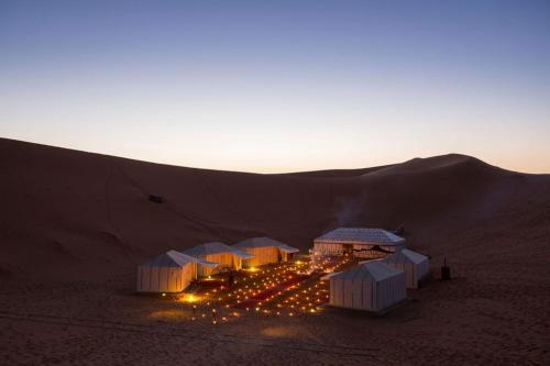 a group of tents in the desert at sunset at loubna merzouga luxury camp in Merzouga
