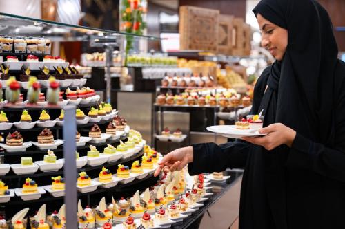 a woman holding a plate of food in a bakery at Swissotel Makkah in Makkah