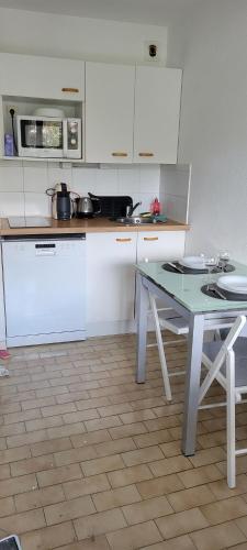 une cuisine avec des placards blancs et une table avec deux chaises dans l'établissement Studio cabine clim rez-de-jardin résid piscine 150 m plage, à La Grande Motte