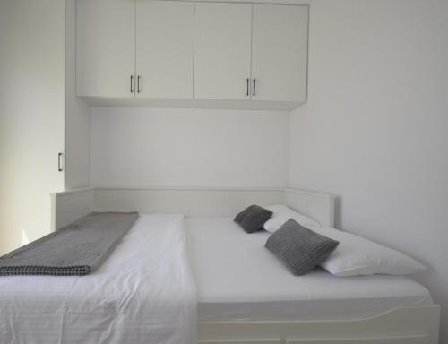 a white bed with two pillows and white cabinets at Apartman Barry in Primošten