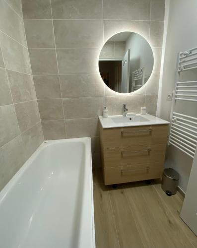 une salle de bain avec une baignoire, un lavabo et un miroir dans l'établissement Appartement Carcassonne résidence capucins, à Carcassonne