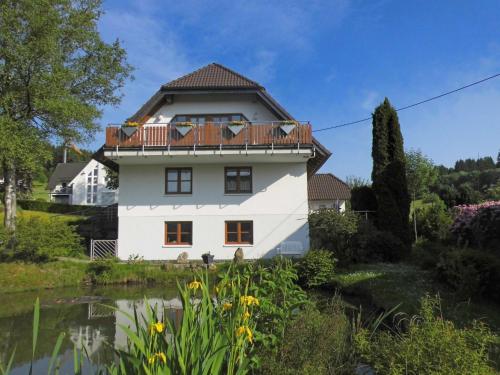 a white house with a balcony and a pond at Cosy apartment with private garden in Brachthausen in the Sauerland in Brachthausen