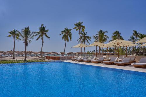 a swimming pool with chairs and umbrellas and palm trees at The Club by Fanar in Salalah