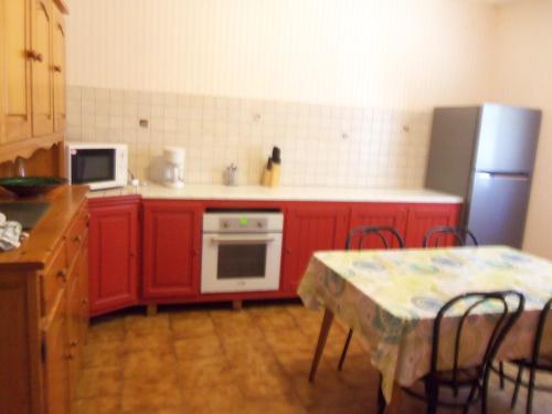La cuisine est équipée de placards rouges, d'une table et d'un réfrigérateur. dans l'établissement Maison a la campagne, à Serres-et-Monguyard