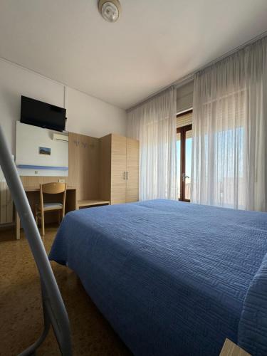 a bedroom with a blue bed and a desk and window at Hotel Ariston in Sottomarina