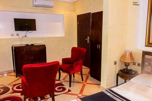 um quarto com cadeiras vermelhas, uma cama e uma televisão em Hôtel LE PÉRIDOT em Brazavile