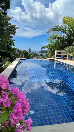 a blue swimming pool with purple flowers in the foreground at Villa Mauao - Luxury Villa in Katamanda, Kata in Kata Beach