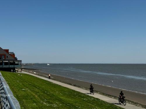 zwei Personen auf einem Bürgersteig neben dem Strand Fahrrad fahren in der Unterkunft Strand-Penthouse, 128 qm, Maisonette, Parkplatz in Wilhelmshaven