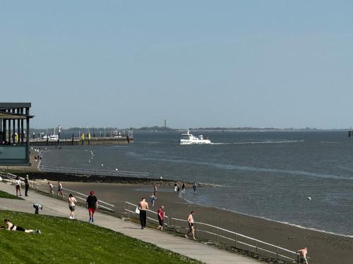 Leute gehen am Strand mit einem Boot im Wasser in der Unterkunft Strand-Apartment, Strandkorb, Meeresrauschen, Parkplatz in Wilhelmshaven