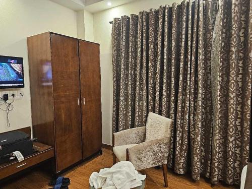 a living room with a curtain and a chair and a cabinet at Hotel Natasha Inn in New Delhi