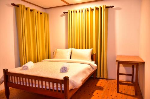 a bedroom with a bed with yellow curtains and a table at Magnolia Hideout in Nuwara Eliya