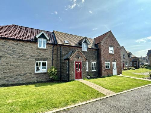 a large brick house with a red door at Nantucket Cottage - Part of the The Bay Filey Holiday Village with pool, gym and direct beach access, pub, restaurant, tennis and meadows walks in Filey