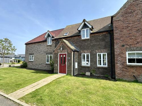 a brick house with a red door and a yard at Nantucket Cottage - Part of the The Bay Filey Holiday Village with pool, gym and direct beach access, pub, restaurant, tennis and meadows walks in Filey